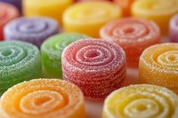 Colorful sugar-coated jelly candy rolls in vibrant orange, yellow, green, purple and pink colors arranged on white surface, macro close-up view showing sweet texture.