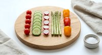 Fresh vegetables arranged in colorful rows on wooden cutting board with cherry tomatoes, cucumber slices, radishes, asparagus and carrots for healthy eating.
