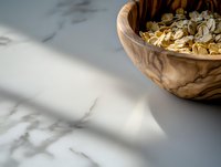 Wooden olive bowl with oats and grains on marble surface in natural morning light casting soft shadows, minimalist breakfast composition with copy space.