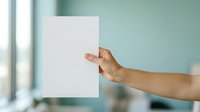 Young adult male with medium skin tone holding blank white paper sheet against soft turquoise background, suitable for mockups, presentations, and advertising campaigns.