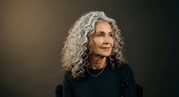 Mature woman with long curly gray hair wearing black clothing against neutral background, professional portrait for mature demographic marketing.