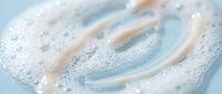 Creamy foam swirl with bubbles on a light blue surface, closeup texture of cleanser or skincare product for beauty and cosmetic design.