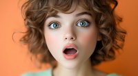 Young woman with bright blue eyes and curly brown hair expressing surprise with open mouth against orange background, beauty portrait in soft lighting.