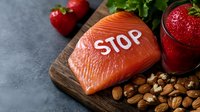 Raw salmon fillet with word Stop carved on surface, served with fresh strawberries, nuts and smoothie on wooden board against dark background.