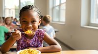 Young African American girl enjoying healthy school lunch in bright cafeteria with classmates in background for educational nutrition campaigns.