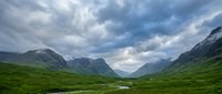 Dramatic mountain valley landscape with lush green meadows, winding river, and moody cloudy sky. Scenic nature background for travel, environment, and outdoor projects.