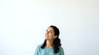 Young woman with long dark hair and glasses, wearing a light blue shirt, looking upward with a thoughtful expression against a white background. Isolated portrait suitable for business, education, and lifestyle design projects.