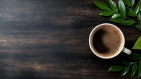 Fresh cup of aromatic coffee with creamy foam on dark wooden background decorated with green leaves, copy space for menu or cafe promotion.