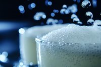 Frothy beer foam with rising bubbles in glass macro shot against dark background with blue bokeh lights, refreshing beverage photography for bar menu design.