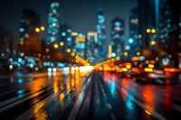 Blurred city street at night with colorful bokeh lights from traffic and buildings creating abstract urban atmosphere on wet asphalt road.