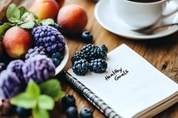 Fresh blackberries, peaches and cup of tea on wooden table with healthy goals written in notebook, morning wellness planning concept with fresh fruits.
