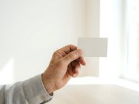 Mature male hand holding blank white card against bright window background, suitable for business card mockups, corporate presentations, and marketing materials.