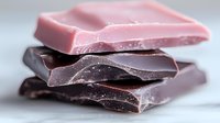 Stack of broken chocolate pieces in varying shades of pink, purple, and dark brown on white background, perfect for dessert or confectionery advertising.