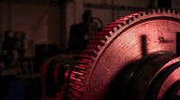 Large industrial gear wheel with detailed teeth in warm red lighting showcasing mechanical engineering and manufacturing precision in factory setting.