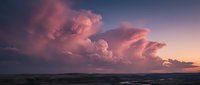 Dramatic storm clouds illuminated in pink and purple hues over ocean waves at sunset creating moody seascape for weather and nature content.