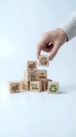 Hand placing wooden blocks with eco-friendly symbols including solar panels, wind turbines, electric cars and recycling icons for sustainable business concepts.