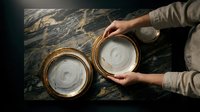 Hands holding ceramic bowls with white glaze on dark marble surface, overhead view for culinary, tableware, and home decor projects.
