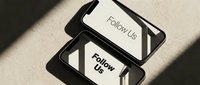 Two modern smartphones displaying Follow Us text on screens, placed on beige surface with dramatic shadows for social media marketing.
