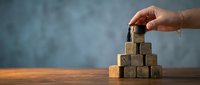 Hand placing wooden cube on pyramid stack representing business growth strategy and leadership development on desk with copy space.