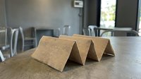 Blank kraft paper tent cards standing on concrete table in modern office space, ready for event names or business messaging.