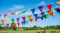 Colorful triangular bunting flags hanging against bright blue sky at outdoor festival or celebration event with people enjoying activities in background.