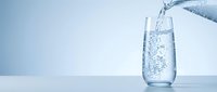 Fresh water pouring from bottle into glass with bubbles and splash on clean blue background for hydration and wellness concepts.