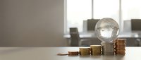 Light bulb on stacked coins representing energy costs, electricity bills, and financial planning for power consumption in modern office setting.