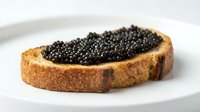 Toasted bread slice topped with creamy spread and luxurious black caviar pearls, served on white plate for gourmet appetizer or fine dining presentation.