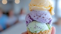 Colorful ice cream scoops stacked in waffle cone with vanilla, berry and mint flavors against blurred cafe background for summer dessert menu designs.