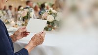 Senior man with weathered hands holding blank white card at elegant event with floral arrangements. Suitable for invitations, announcements, greetings.