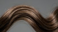 Flowing brown hair strand with natural highlights creating elegant wave pattern against neutral background for beauty and haircare concepts.