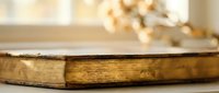 Vintage antique book with golden pages and worn leather binding resting on wooden surface in soft natural light creating warm atmospheric mood.