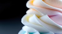Soft foam waves in delicate pastel colors create abstract layered pattern on dark background. Gentle curves and folds showcase smooth texture and gradient transitions.