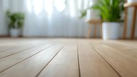 Wooden floor planks in modern bright interior with blurred background of houseplants and furniture. Natural light through sheer curtains creates cozy atmosphere.