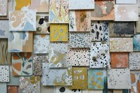 Abstract geometric wall composition featuring layered square tiles with paint splatter patterns in muted earth tones, blues, and yellows creating artistic texture.