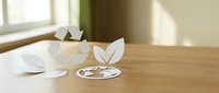 Paper cut recycling symbol, green leaves, and globe on wooden table in sunlit room, representing eco-friendly sustainability and environmental awareness.