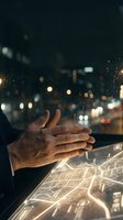 Male hand with medium skin tone interacting with glowing digital holographic map interface against blurred nighttime cityscape. Urban technology and navigation concept.