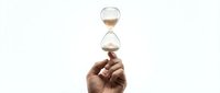 Hand holding hourglass with flowing sand against white background, symbolizing time management, deadline pressure, and business productivity concepts.