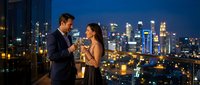 Elegant couple enjoying champagne on luxury rooftop terrace with stunning city skyline at night, perfect for romantic dinner date celebration.