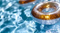 Golden inflatable ring floating on sparkling blue swimming pool water with sunlight reflections creating magical ripple patterns and bokeh effects.