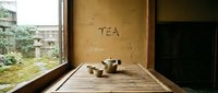 Ceramic tea set on bamboo tray in minimalist Asian interior with garden view and rustic wall inscription, evoking calm and tradition.