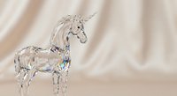 Crystal glass unicorn figurine with rainbow reflections on soft beige fabric background. Decorative mythical creature ornament for fantasy and magic themes.