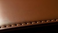 Brown leather material with decorative stitching detail showing craftsmanship and texture for luxury goods manufacturing and fashion design projects.