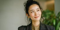 Young Asian businesswoman smiling confidently in modern office environment with natural lighting and green plants in background for corporate presentations.