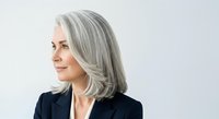 Middle-aged woman with long silver gray hair, fair complexion, wearing dark blazer against white background. Professional portrait for business, corporate, and lifestyle design projects.