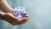 Cupped hands holding glowing holographic scales of justice symbol representing legal protection, law services, and balanced decision making in business.