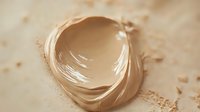 Smooth swirl of liquid foundation makeup or bb cream on beige background with powder texture, showing cosmetic product consistency and color tone.