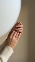 Two women's hands stacked together showing unity, support and teamwork. One hand wears a gold ring. Neutral beige background with soft natural lighting for partnership and collaboration concepts.