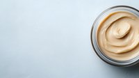 Creamy peanut butter in glass jar with smooth swirl texture on light background for cooking and breakfast recipes.
