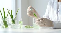 Scientist in white lab coat conducting plant research with green leaves in glass containers for botanical laboratory experiments and natural medicine development.